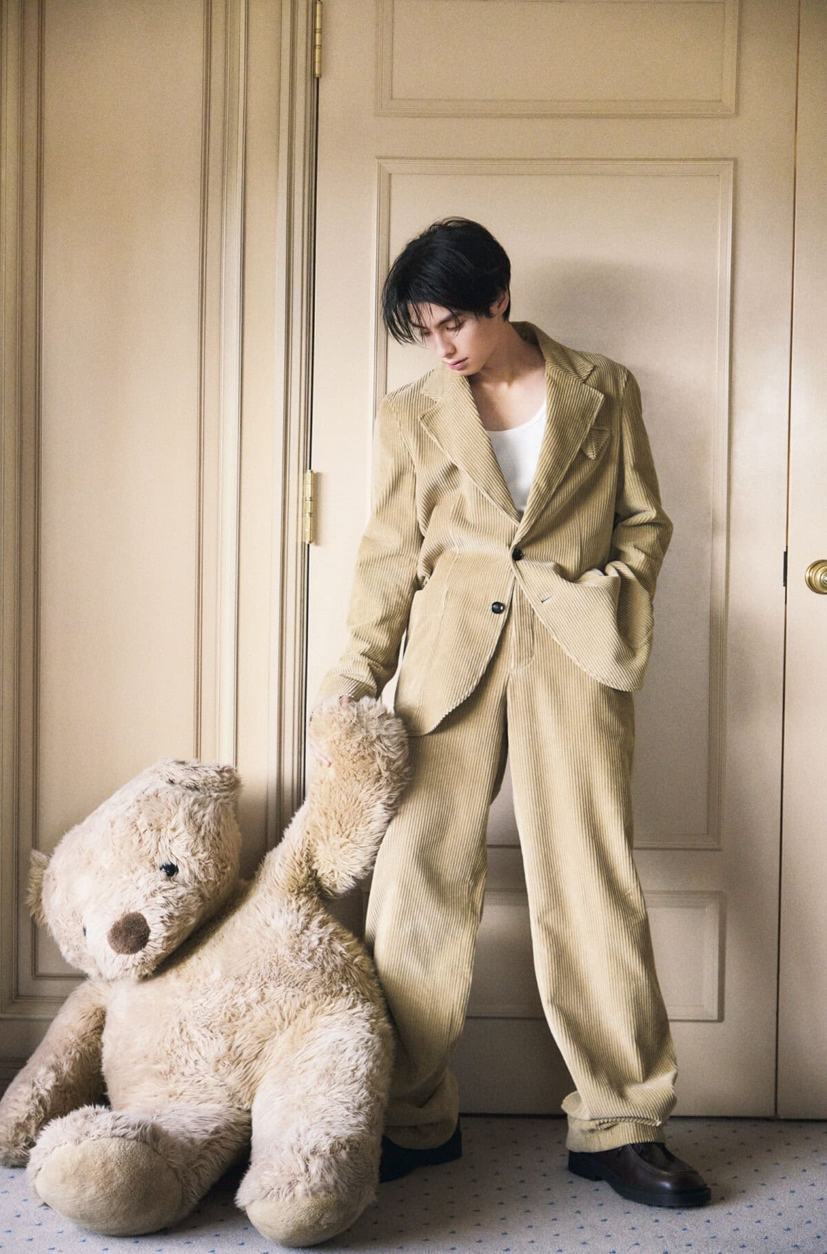 本田響矢がコーデュロイのスーツ姿で、ぬいぐるみに手を伸ばすホリデイ撮影シーン