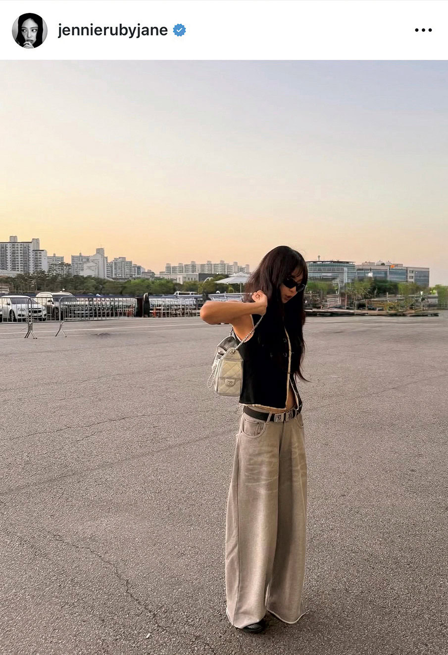 BLACKPINKジェニーの公式Instagram投稿より。黒のタイトなジレ調のクロップドトップスからヘルシーにお腹を覗かせ、ルーズなベージュのワイドデニムパンツとシャネルのシルバーのチェーンバッグを合わせた、最旬の「腹チラ×ずるボトム」スタイル。