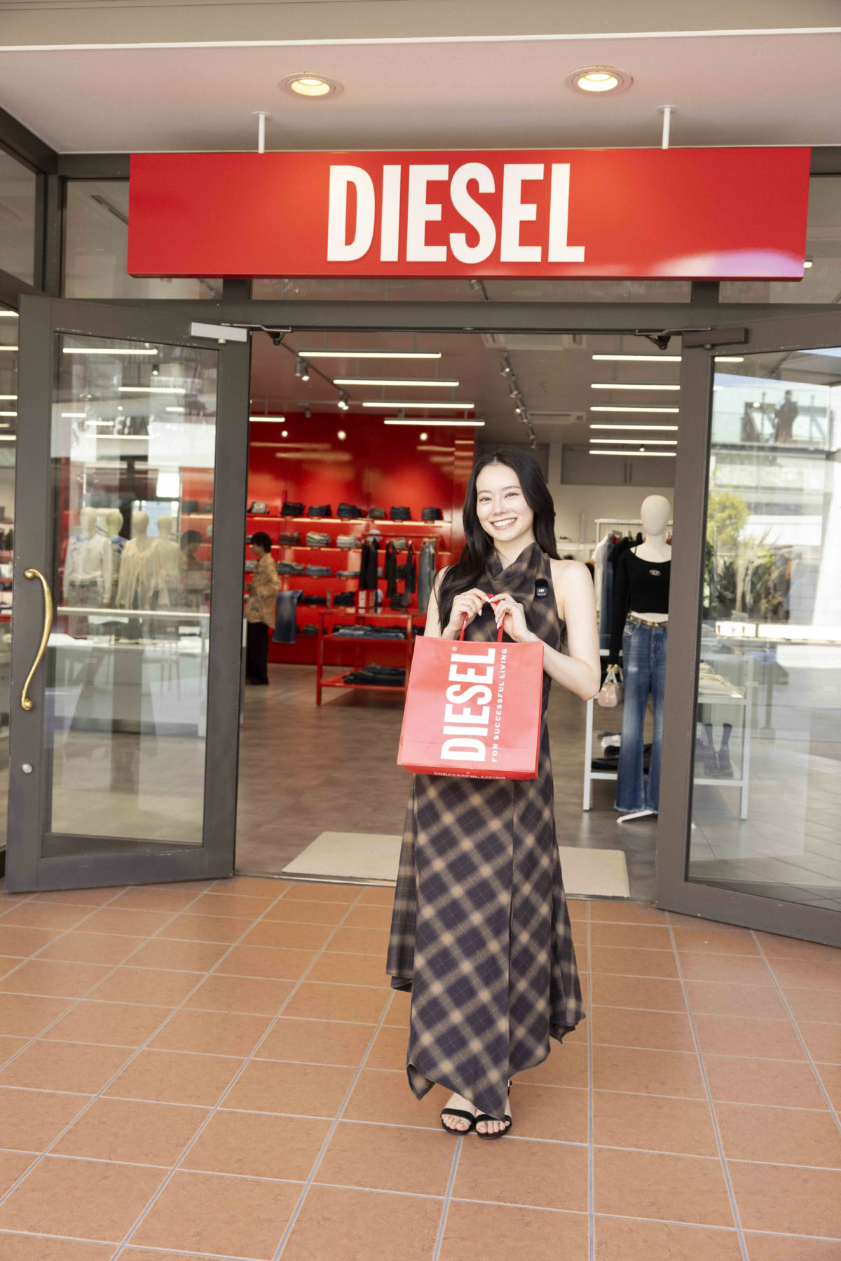 DIESELの赤と白のショップバッグを手に店頭でキュートに微笑むなごみちゃん