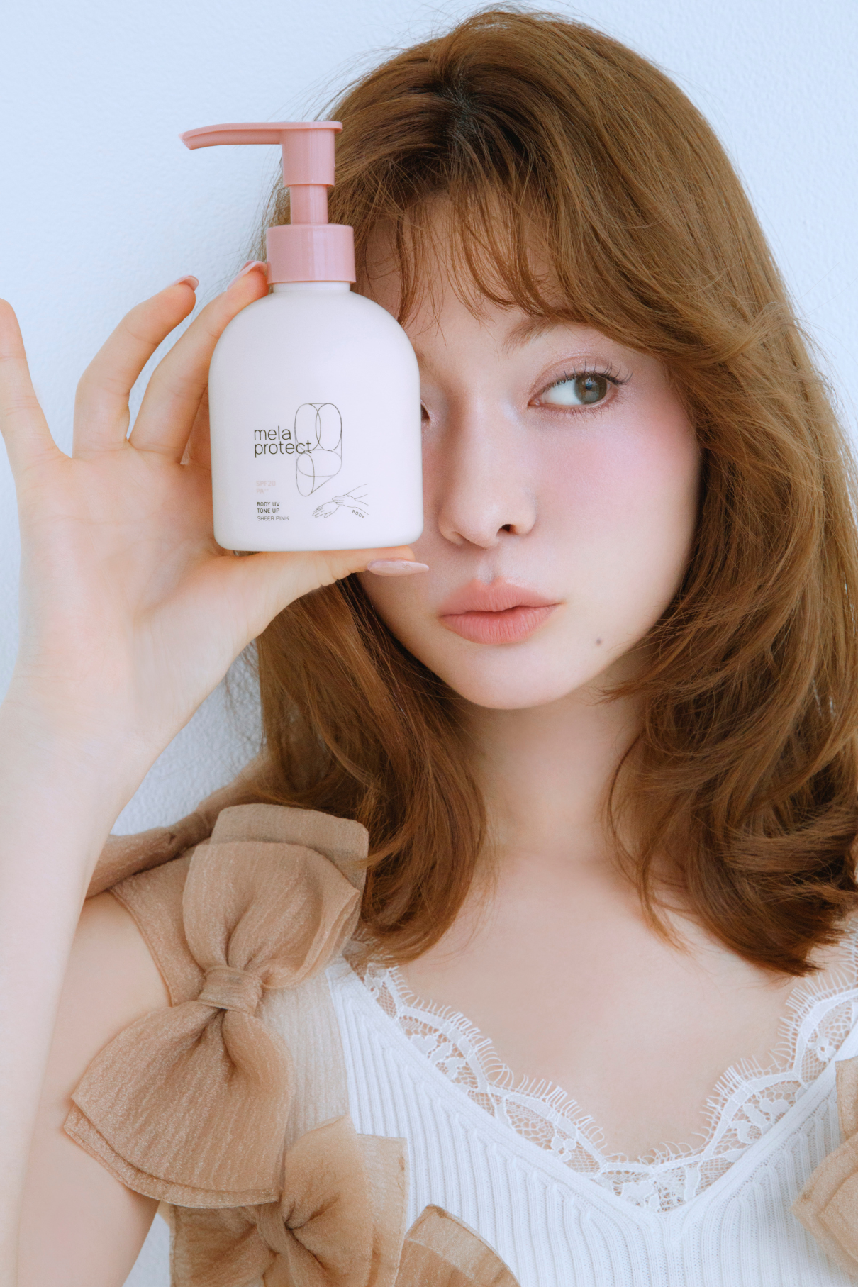 メラプロテクト ボディUV トーンアップのボトルを持ち、ポーズをとる八木アリサさんのカット。