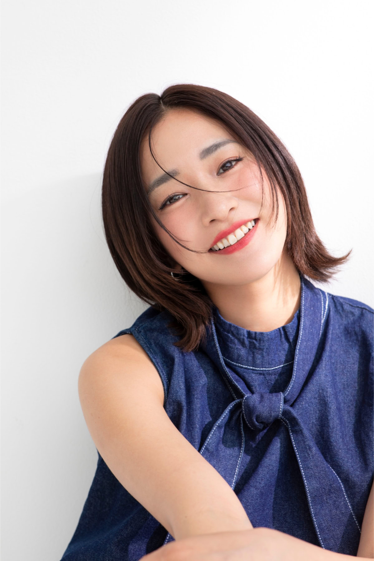 平川愛里菜さんの上半身ポートレート。ネイビーのノースリーブトップスを着用し、首元のリボンデザインがアクセントになっている。ショートボブヘアを自然に下ろし、やわらかな光が差し込む室内で首を少し傾けながら明るい笑顔を見せている。親しみやすさと洗練された雰囲気が印象的な一枚。