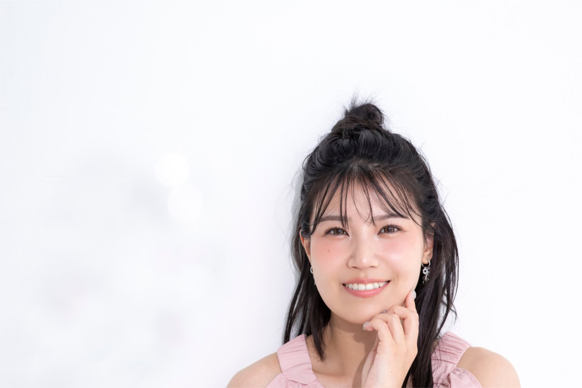 ポコチャライバーのなるごりさんが淡いピンクのオフショルダーワンピースを着て白い壁際に座り、やわらかな笑顔を見せているポートレート写真