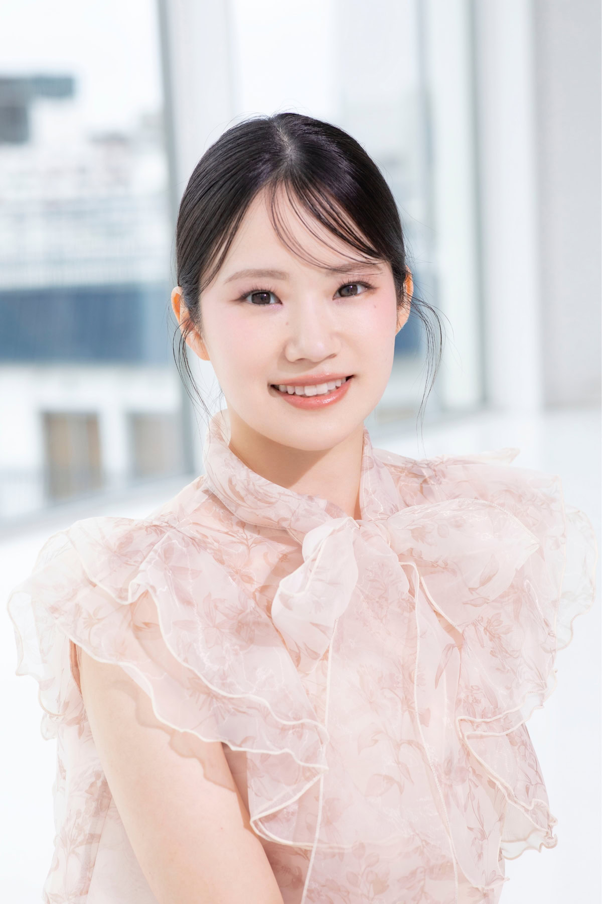 あきのさんが淡いピンクの花柄ブラウスを着用し、明るい室内でカメラに向かって微笑んでいるポートレート写真。