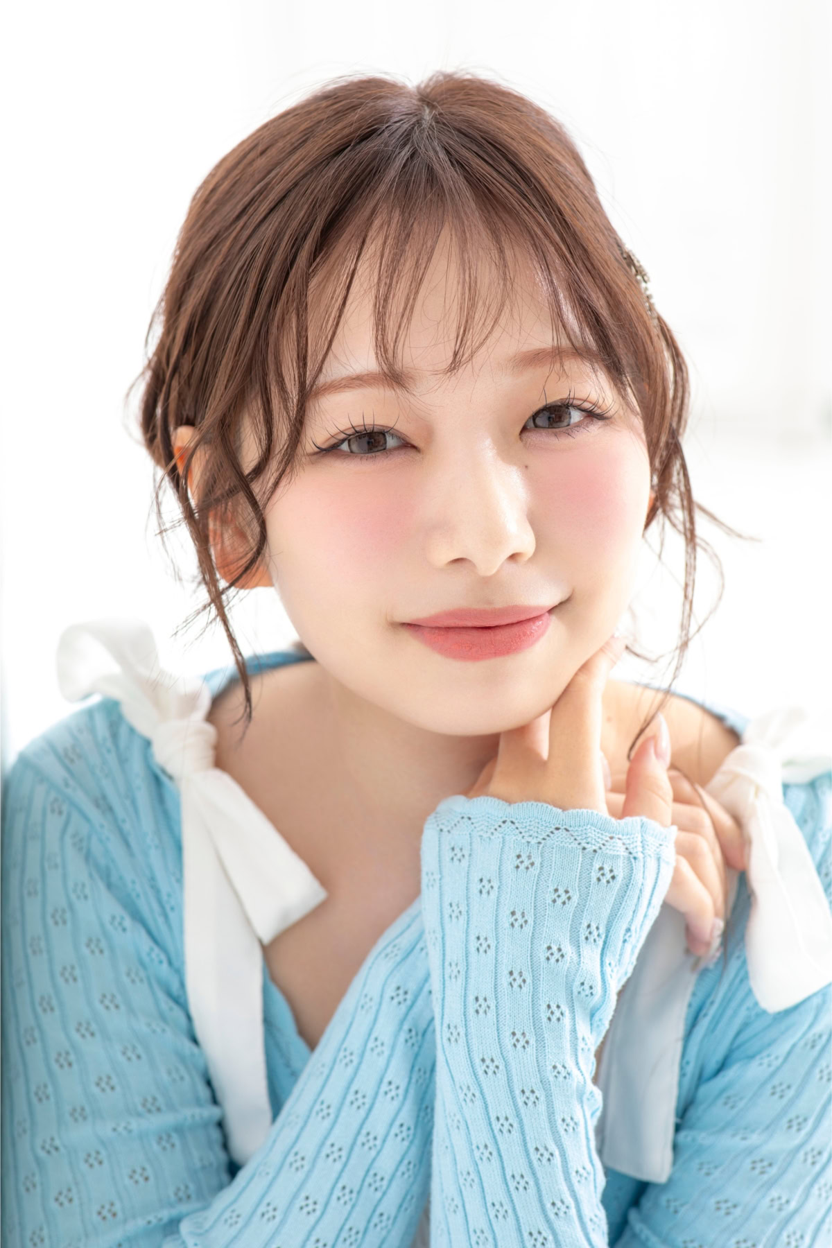 白身魚ちゃんさんの顔寄りのポートレート。淡いブルーのニットトップスを着用し、肩の白いリボンがアクセントになっている。頬に手を添えながらカメラを見つめ、やわらかな自然光の中で優しい微笑みを浮かべている。透明感のある雰囲気とナチュラルな表情が印象的。