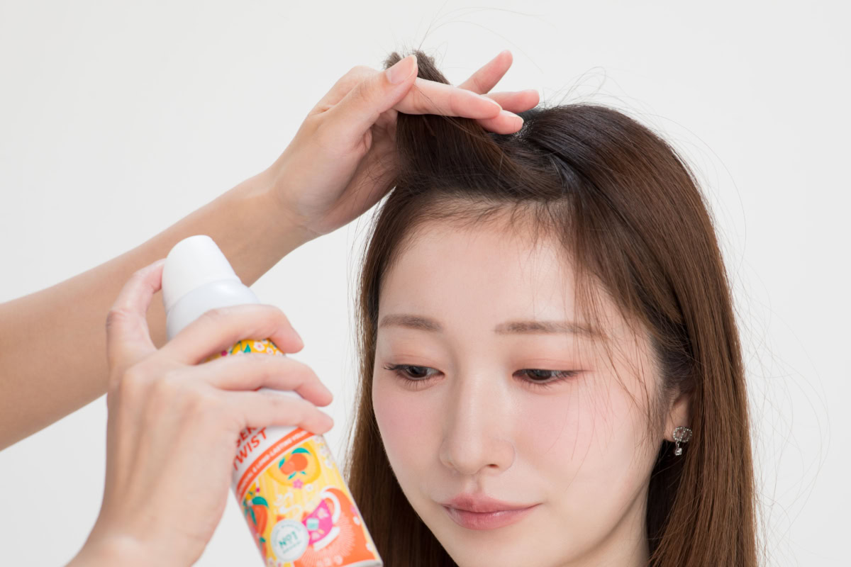 前髪を上げて根元を露出させ、30cmほど離した位置からドライシャンプー「バティスト」をスプレーする様子