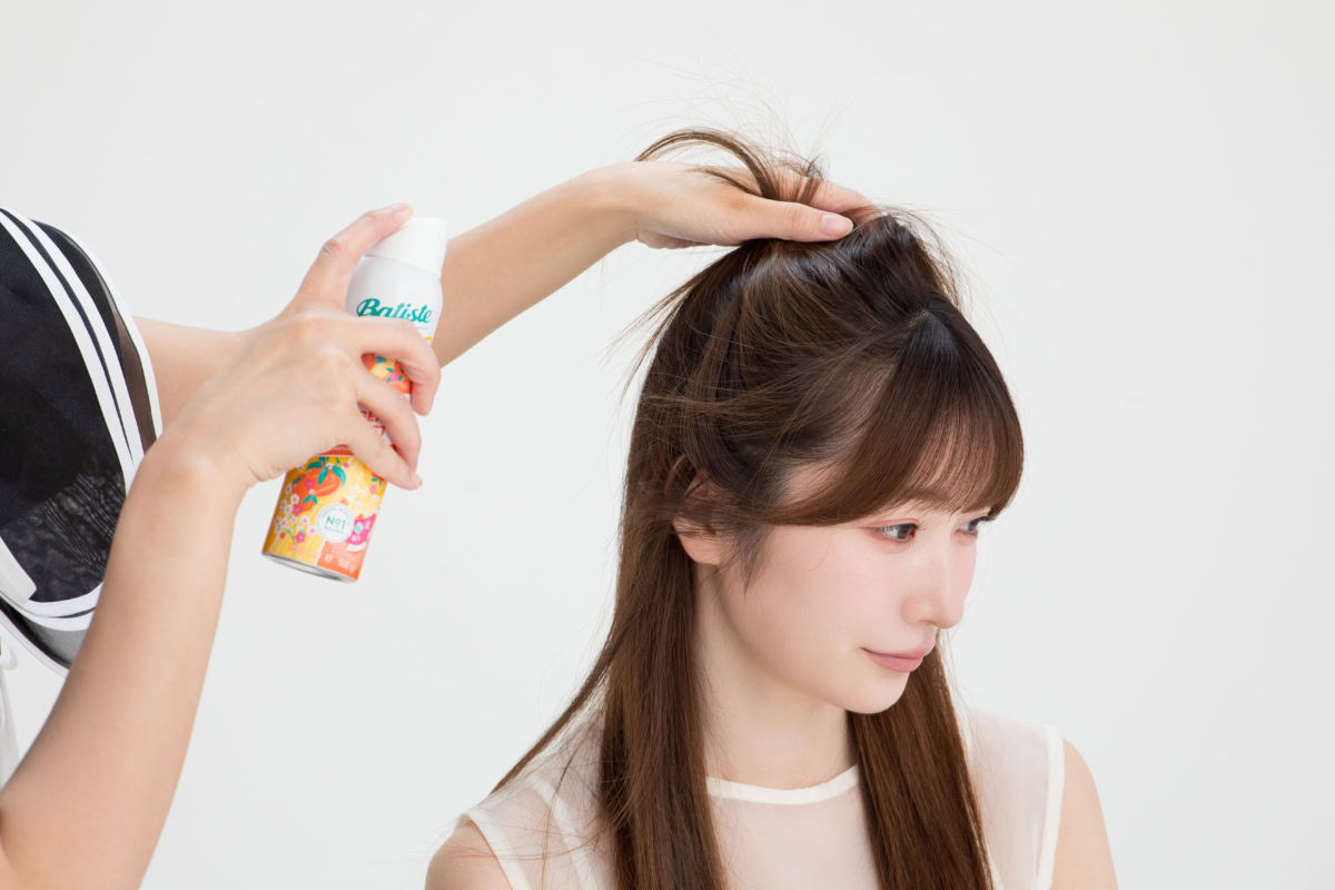 トップの髪をかき上げて内側を露出させ、根元を狙ってドライシャンプー「バティスト」をスプレーする様子