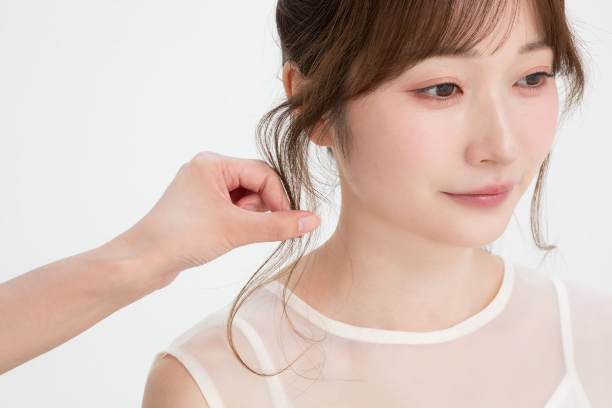 耳前の後れ毛の根元から毛先にかけて指先を滑らせ、パウダーをなじませながらきれいなカーブを作る仕上げ