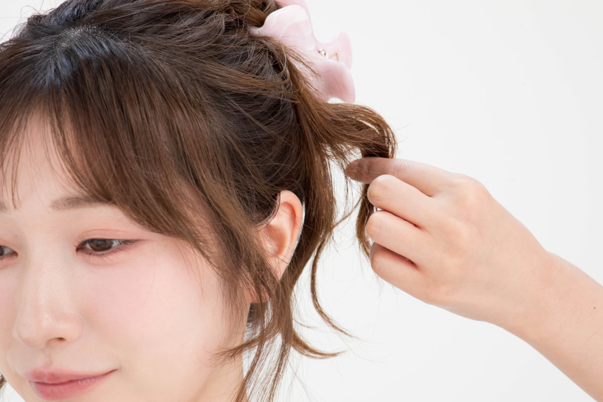 ピンクのリボンクリップでまとめた髪の毛先を指先でつまみ上げ、立体感を出していくスタイリングの様子