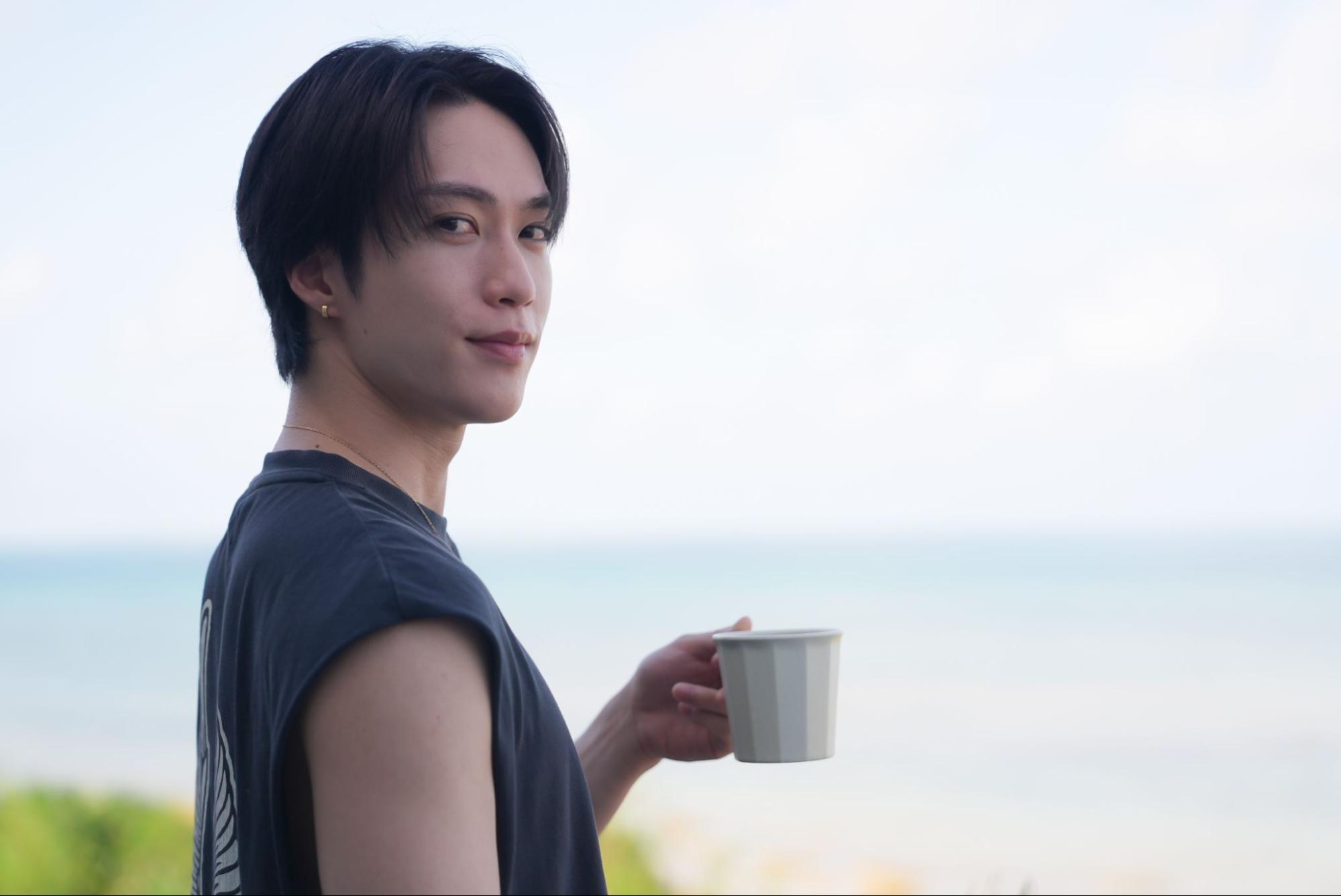 男性が、八重山の海を眺めながらフローティングブレックファストを楽しむ様子。コーヒーカップを片手にカメラを振り返るカット