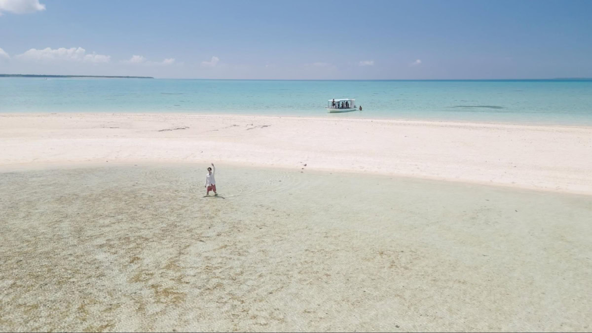 小浜島周辺の海に浮かぶ真っ白な砂浜の「幻の島」 で、男性が遠くから手を振る様子