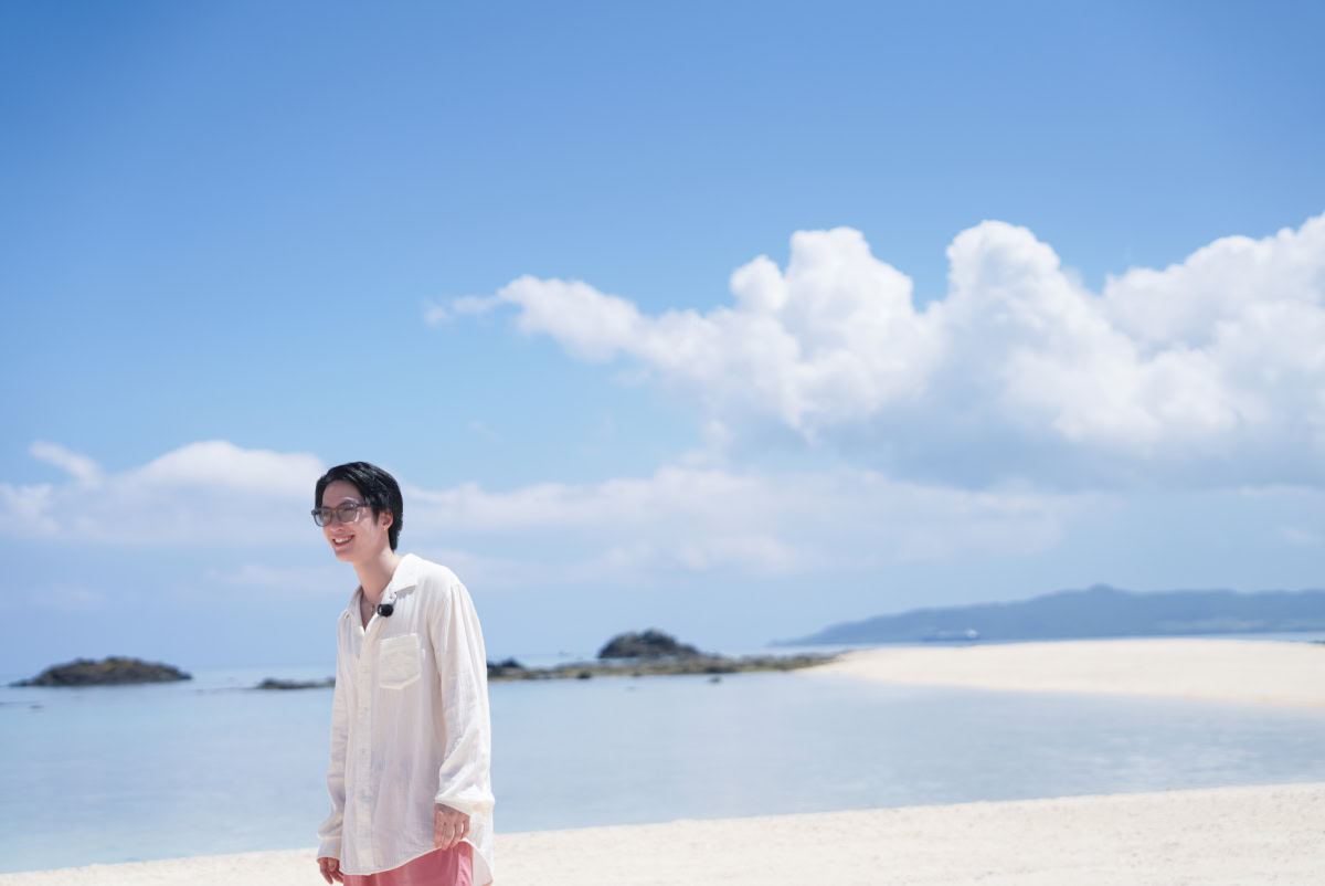 「幻の島」の白い砂浜で、青い空をバッグに海を眺めるTHE RAMPAGE 藤原樹さん