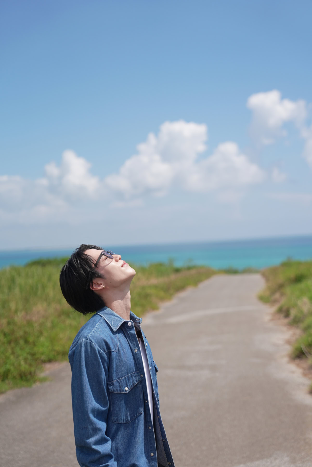 小浜島で青空をバックに、男性が空を見上げて目を瞑り、自然を感じている様子