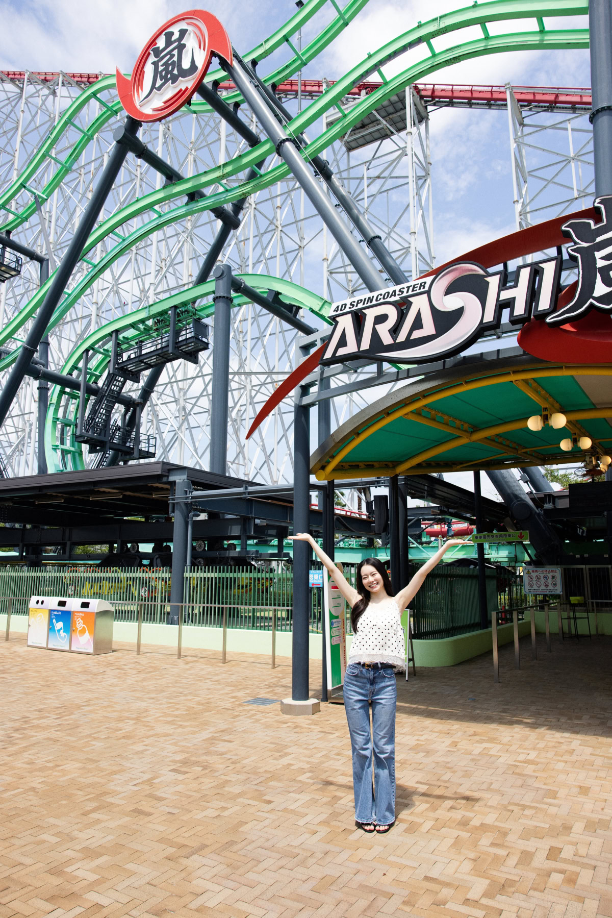 4Dスピンコースター『嵐 (ARASHI)』の大型ロゴ看板の前で手を大きく広げてポーズをとるなごみちゃん